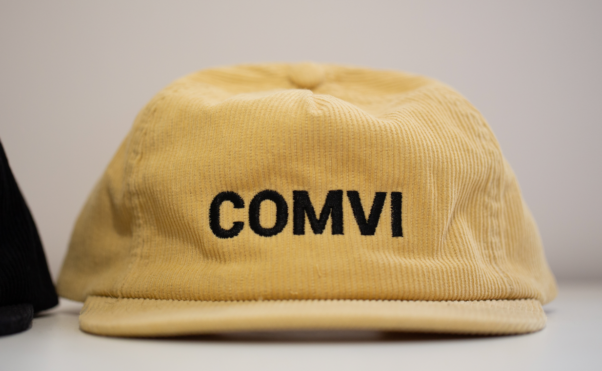 Beige cap with 'COMVI' text on a light gray background