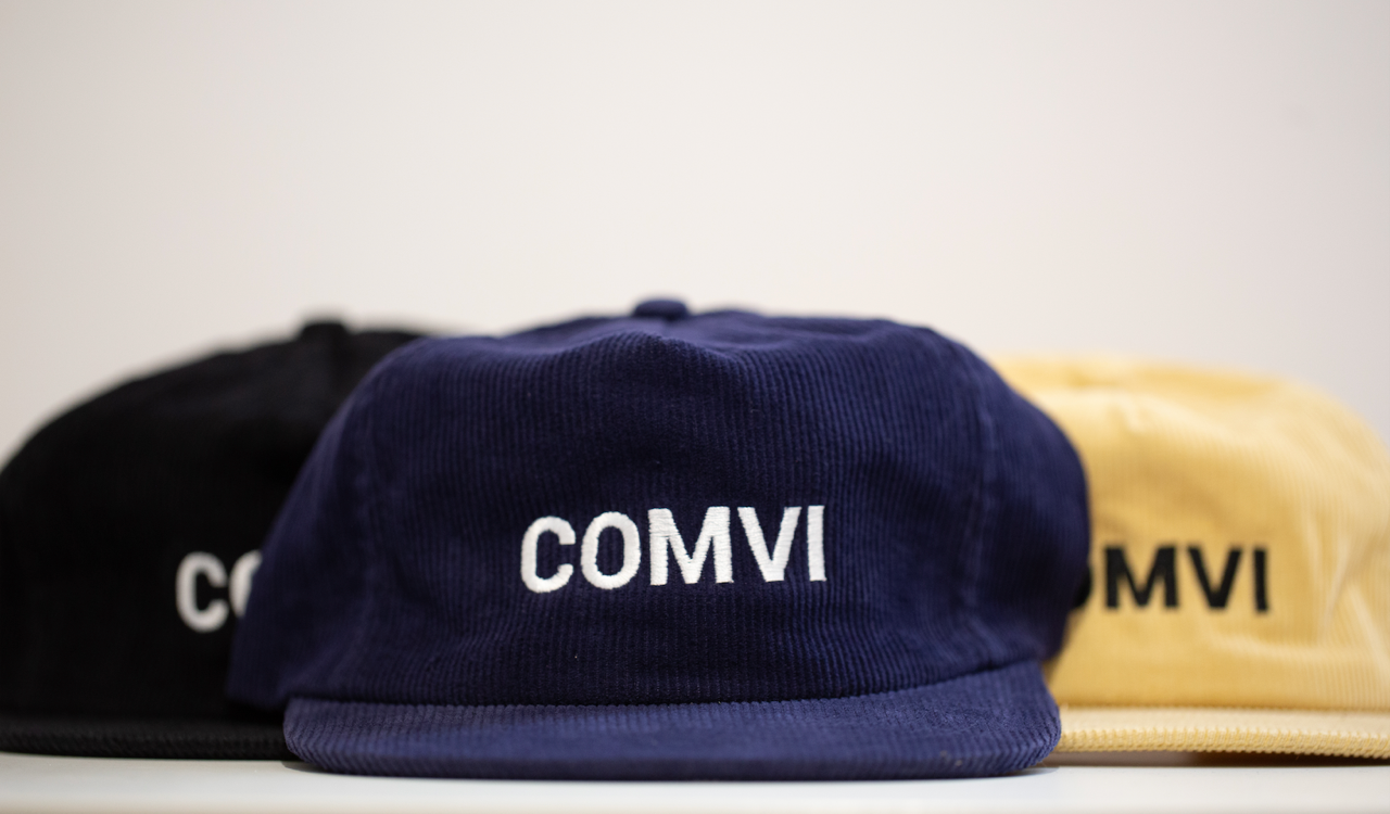 Three caps with 'COMVI' branding on a light background