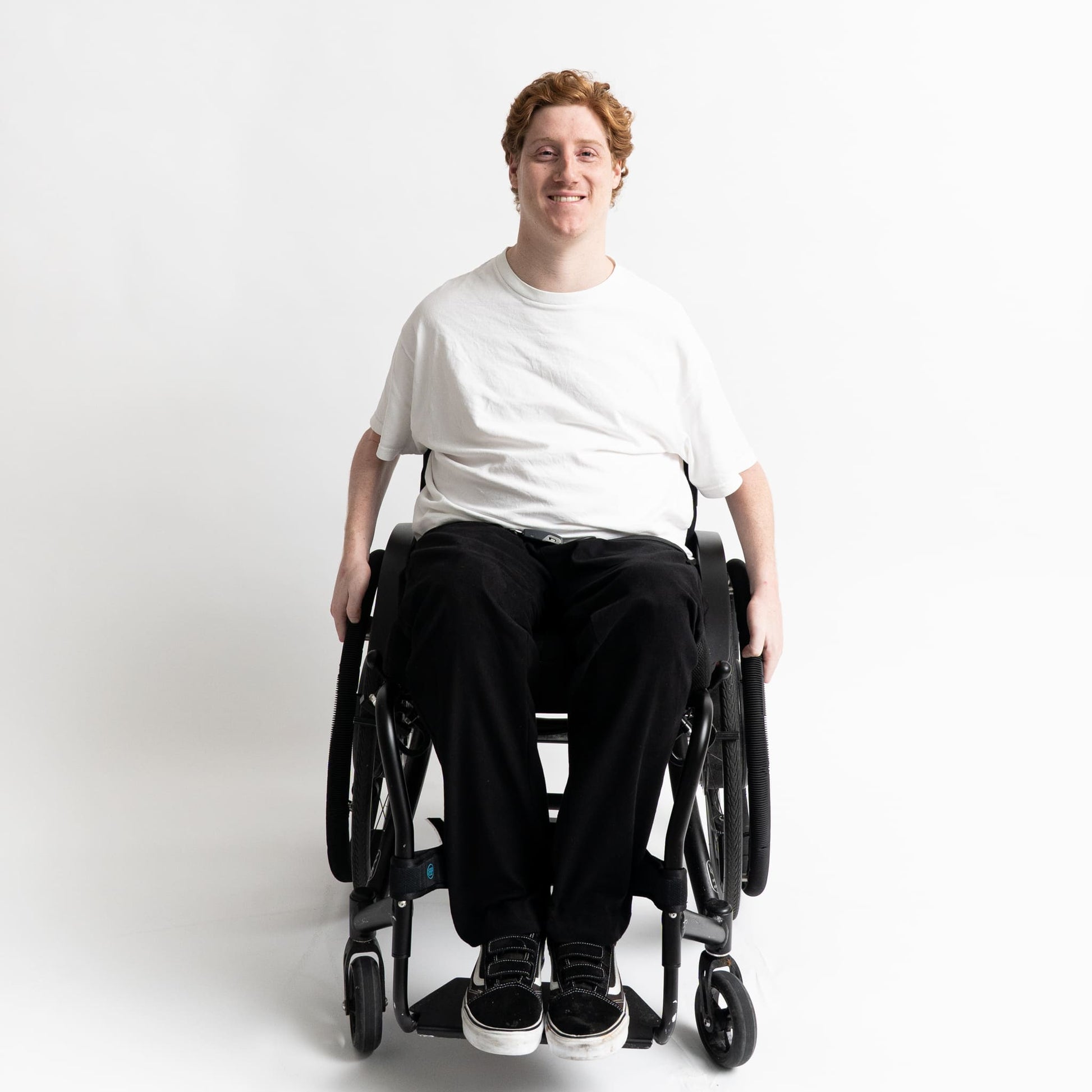 Model seated in a wheelchair wearing adaptive straight-leg pants in black with accessible pockets and elastic waistband.”