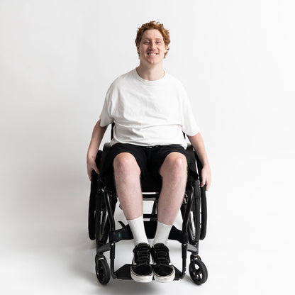 Model seated in a wheelchair wearing adaptive cotton shorts with elastic waist and front-access pockets.